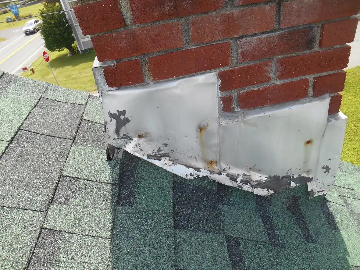 Failed, patched flashing where a chimney meets the shingle roof